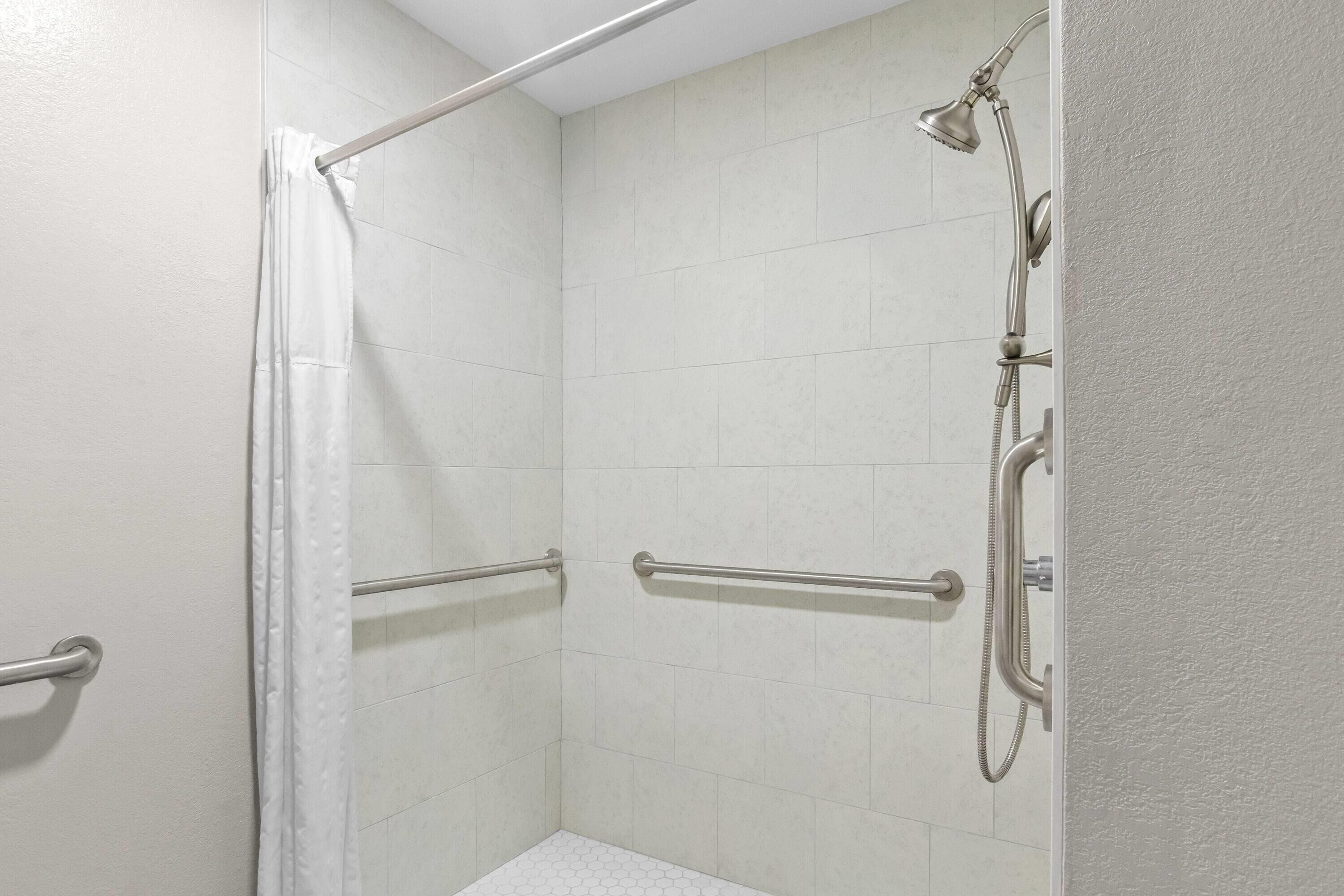 A shower area with a white tiled wall, a showerhead, a handheld shower attachment, and a grab bar.