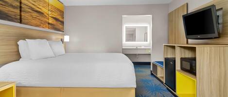 A hotel room with a large bed, a TV mounted on a wooden cabinet, a window with a view, and a painting on the wall.