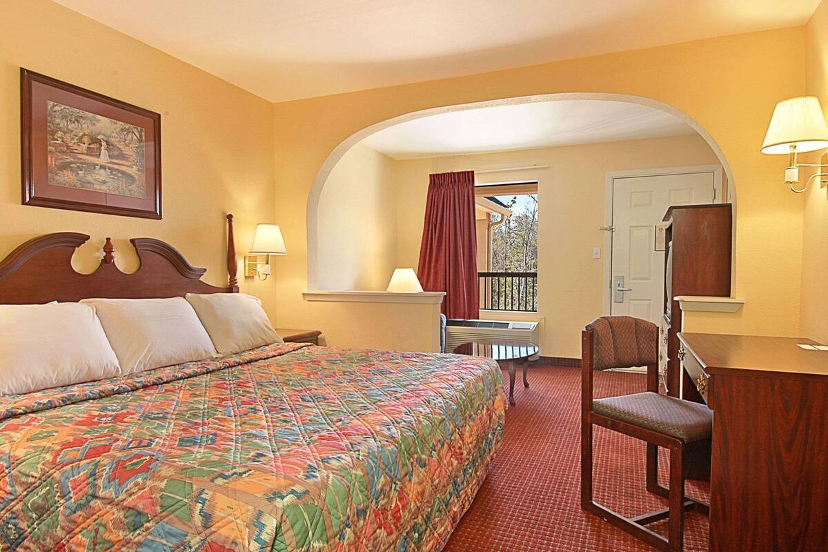 A hotel room with a bed, a desk, a chair, a window with curtains, and a door.