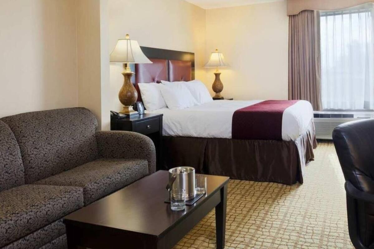 A hotel room with a bed, a sofa, a table, lamps, and a window with curtains.