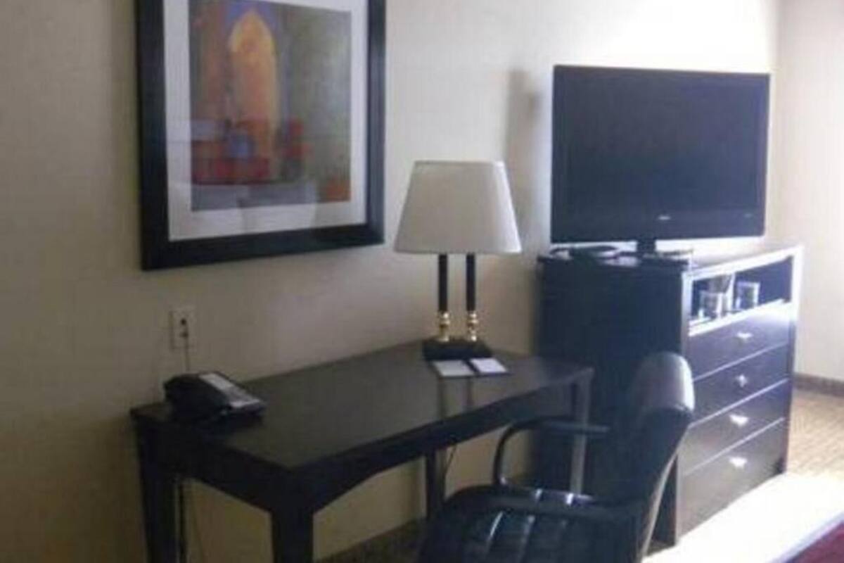 A hotel room with a desk, chair, television, lamp, and a framed picture on the wall.