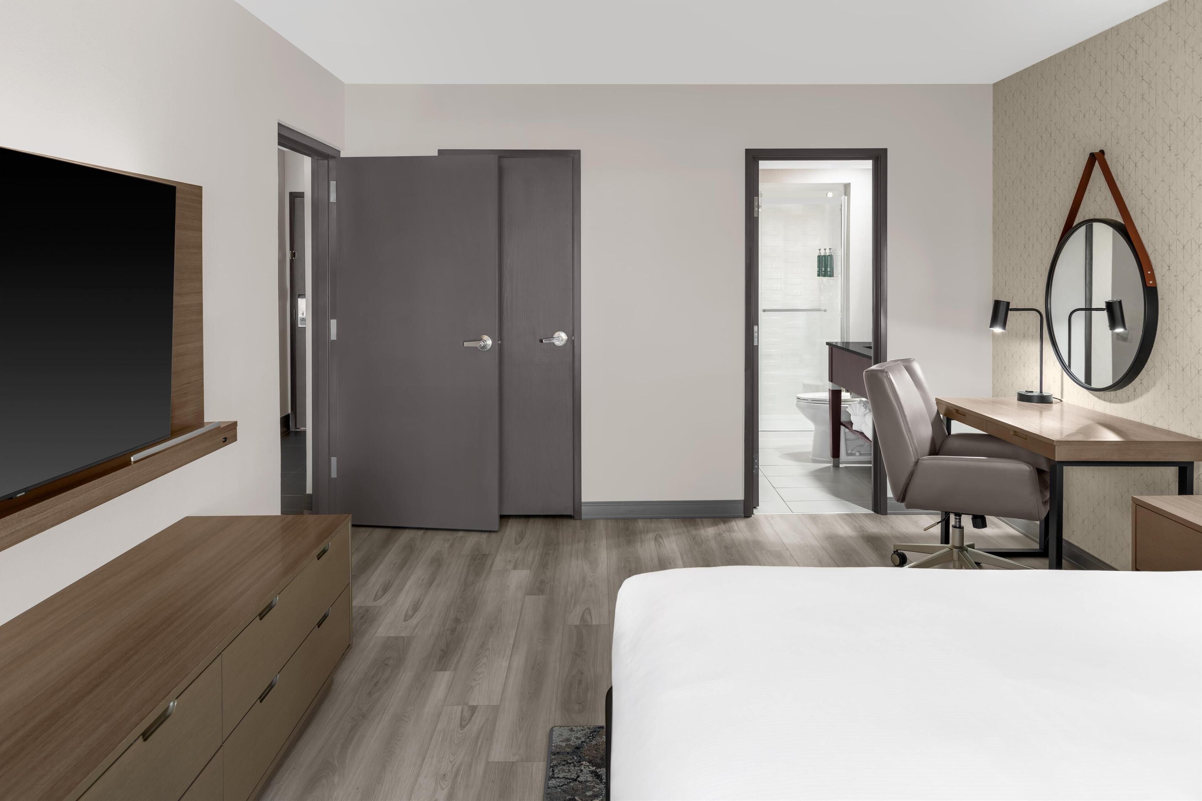 Habitación de hotel moderna con cama, escritorio, silla, televisor y armario.