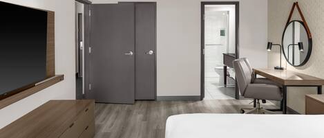 Habitación de hotel moderna con cama, escritorio, silla, televisor y armario.