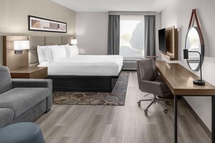Habitación de hotel con una cama grande, un escritorio, una silla, un televisor y una ventana con cortinas.