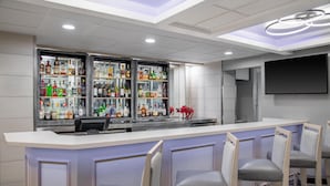 A bar area with a counter, multiple shelves of bottles, and bar stools. - DoubleTree by Hilton Springdale (Springdale)