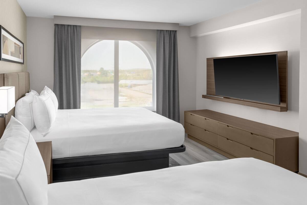 A hotel room with a large bed, a TV mounted on the wall, and a view of the outdoors through a large window.