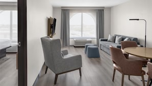 A modern living room with a grey armchair, a grey sofa, a round table with chairs, and a large window with curtains. - DoubleTree by Hilton Springdale (Springdale)