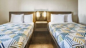 Et hotelværelse med to enkeltsenge, hver med et mønstret sengetæppe, en træhovedgærde og et natbord med en lampe.
