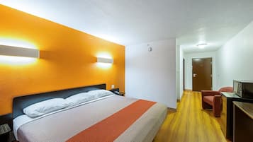 A hotel room with a bed, a desk with a computer, and a door in the background.