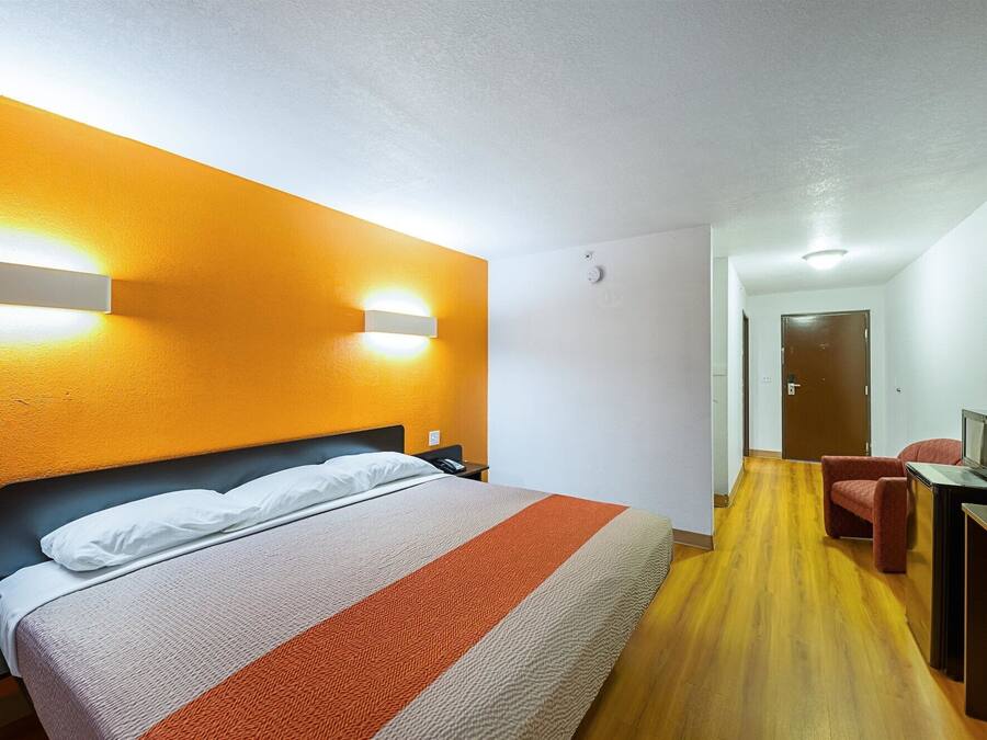A hotel room with a bed, a desk with a computer, and a door in the background.