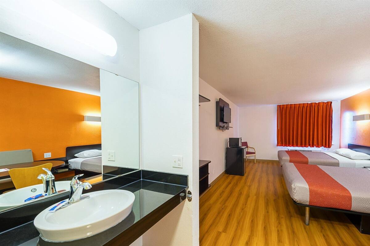 A hotel room with a large mirror, two beds, a TV, and a wooden floor.
