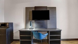 Et moderne værelse med et fladskærms-tv på væggen, et skrivebord med stol og en mikrobølgeovn til venstre.