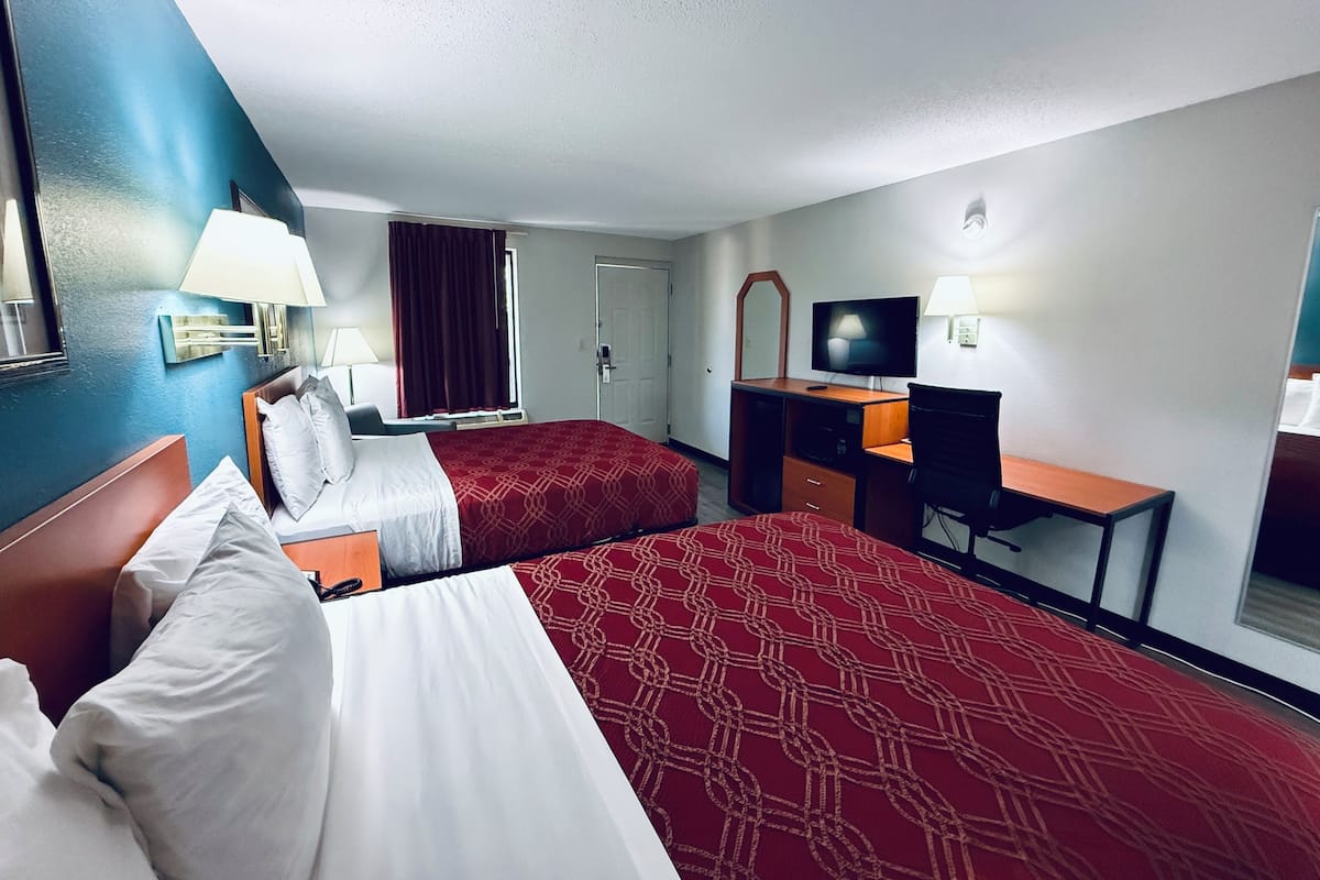 A hotel room with two beds, a desk, a TV, and a mirror.