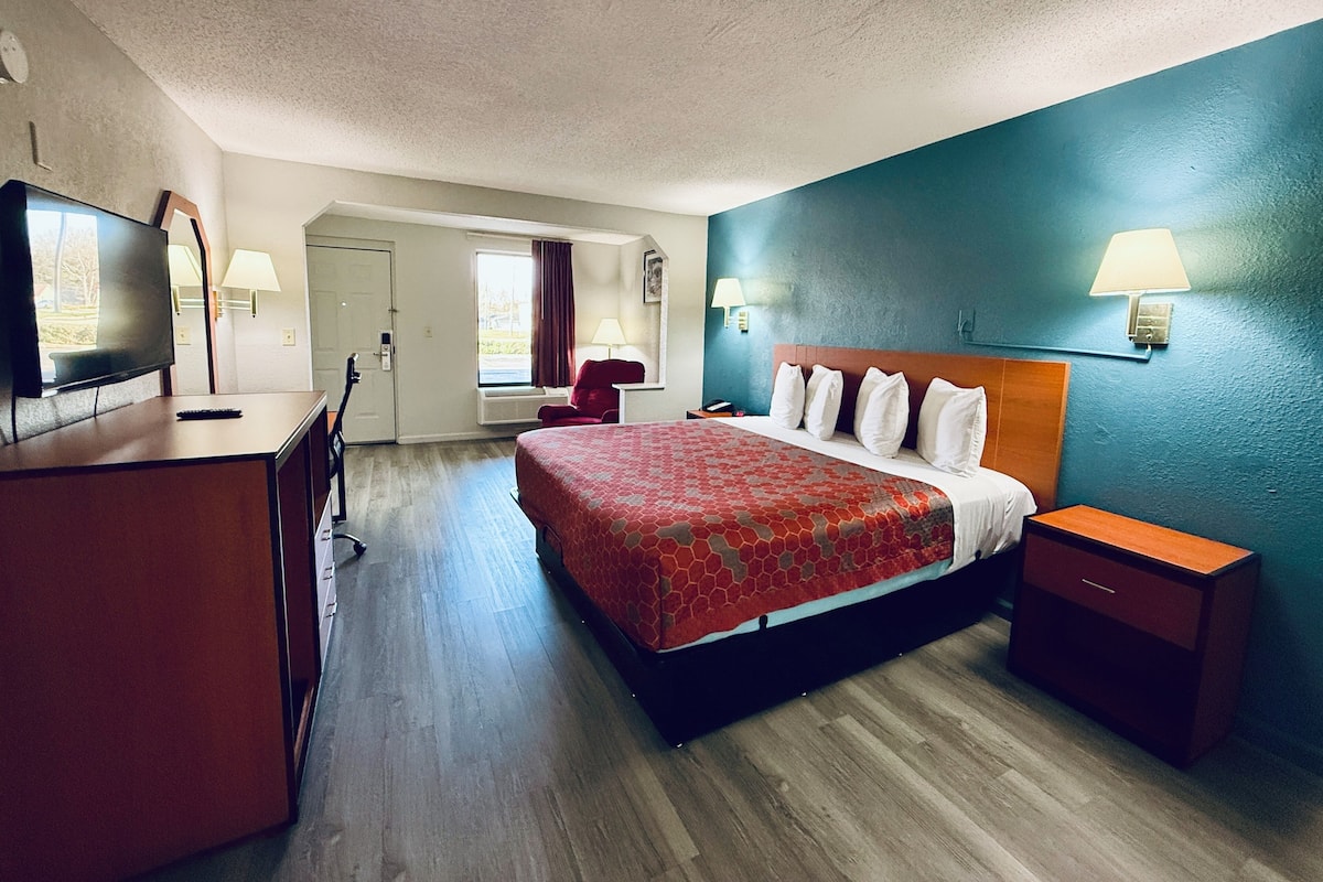 A hotel room with a bed, a desk, a TV, and a window.