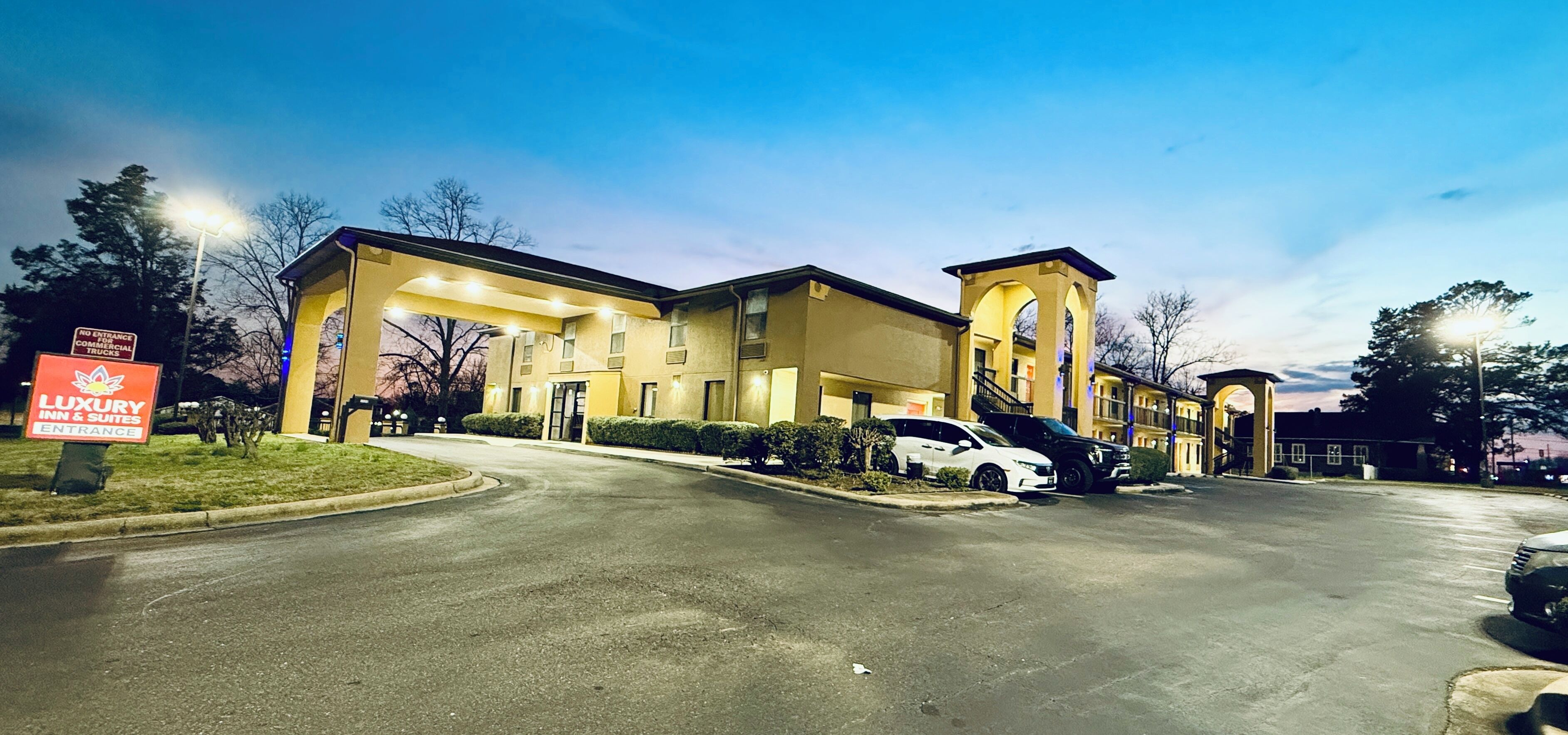 A hotel with a gated entrance, a sign for 'Luxury Inn & Suites,' and a parking lot with cars.