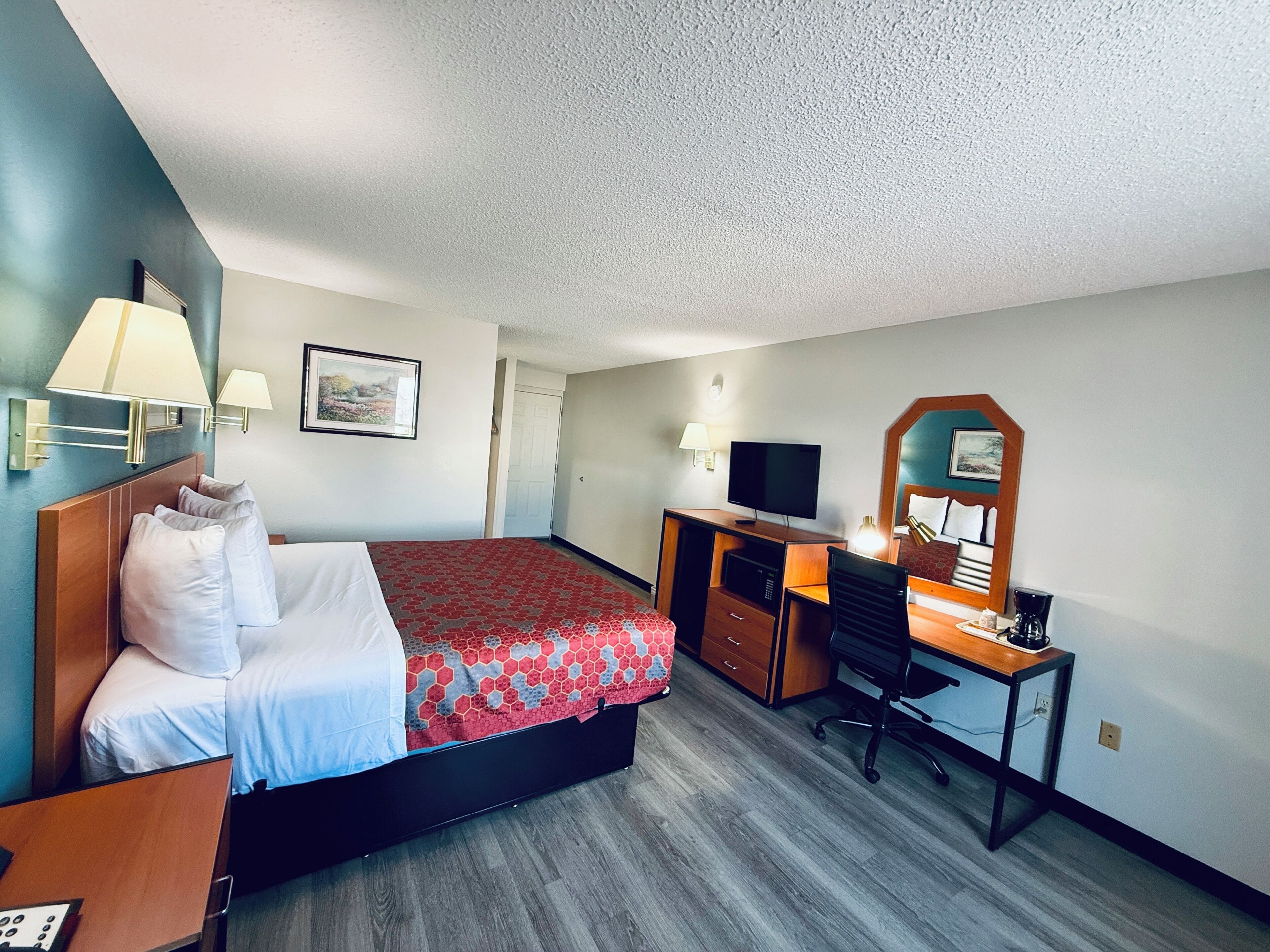 A hotel room with a bed, desk, chair, television, and a mirror.