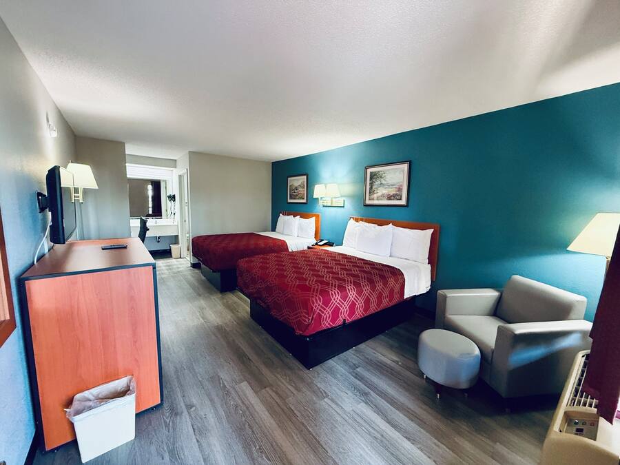 A hotel room with two beds, a desk, a chair, and a waste bin.