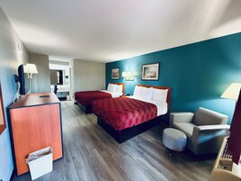 Habitación de hotel con dos camas, un escritorio, una silla y un cesto de basura.