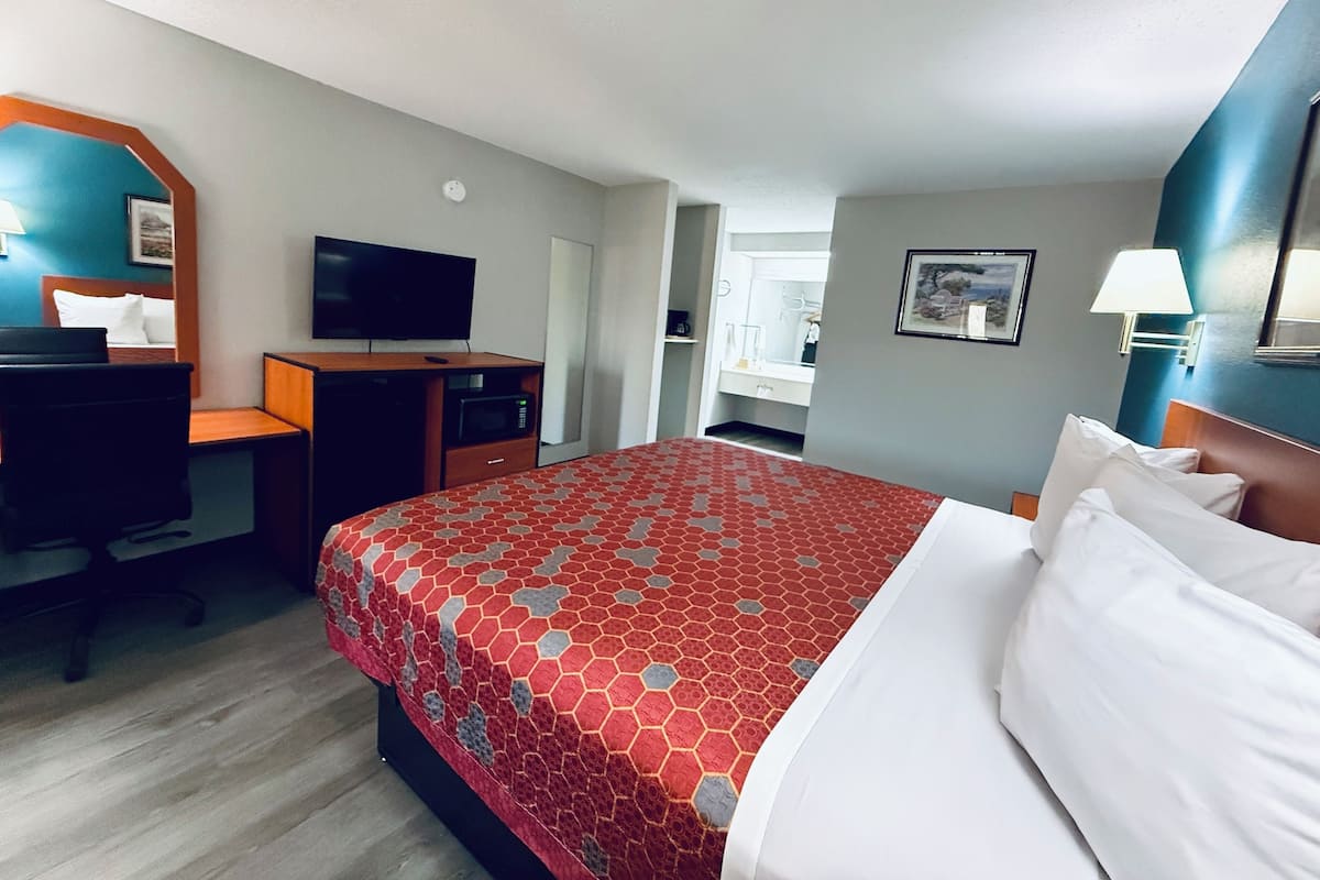A hotel room with a bed, a desk, a TV, a microwave, and a bathroom visible through an open door.