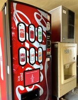 Máquina expendedora de Coca-Cola con varias opciones de bebidas y un dispensador de hielo adyacente.