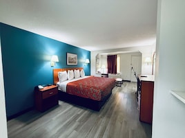 Una habitación de hotel con una cama, mesitas de noche, un escritorio, una silla y un espejo.