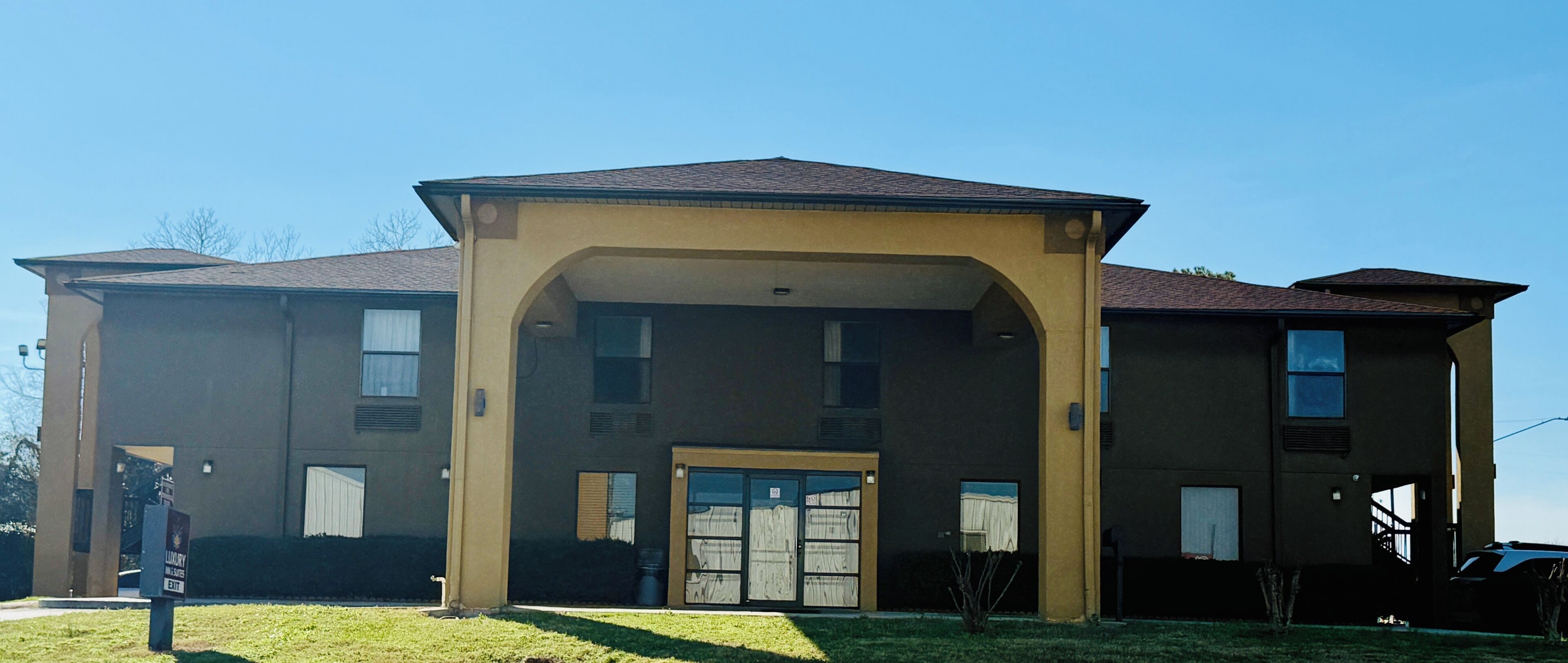 Un edificio de dos pisos con un porche cubierto, varias ventanas y techo plano.
