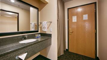 A hotel bathroom with a sink, mirror, towel rack, and a wooden door.