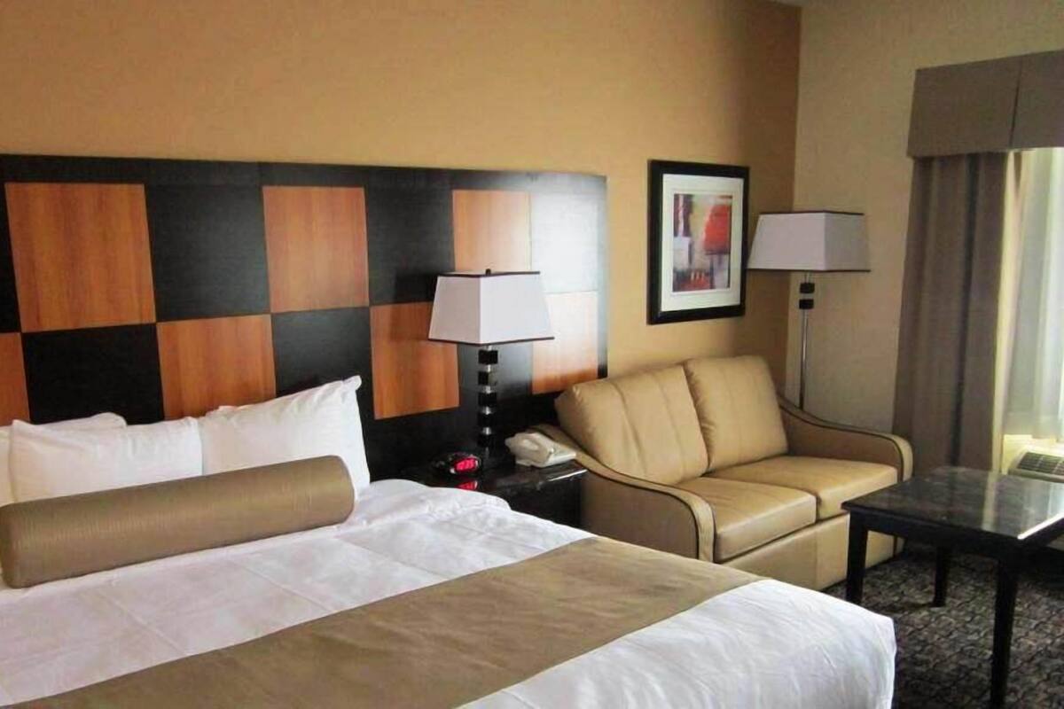 A hotel room with a large bed, a desk, a chair, and a lamp.