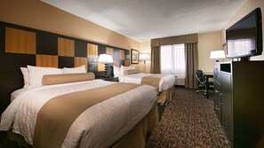 A hotel room with two beds, a desk, a television, and a window with curtains.