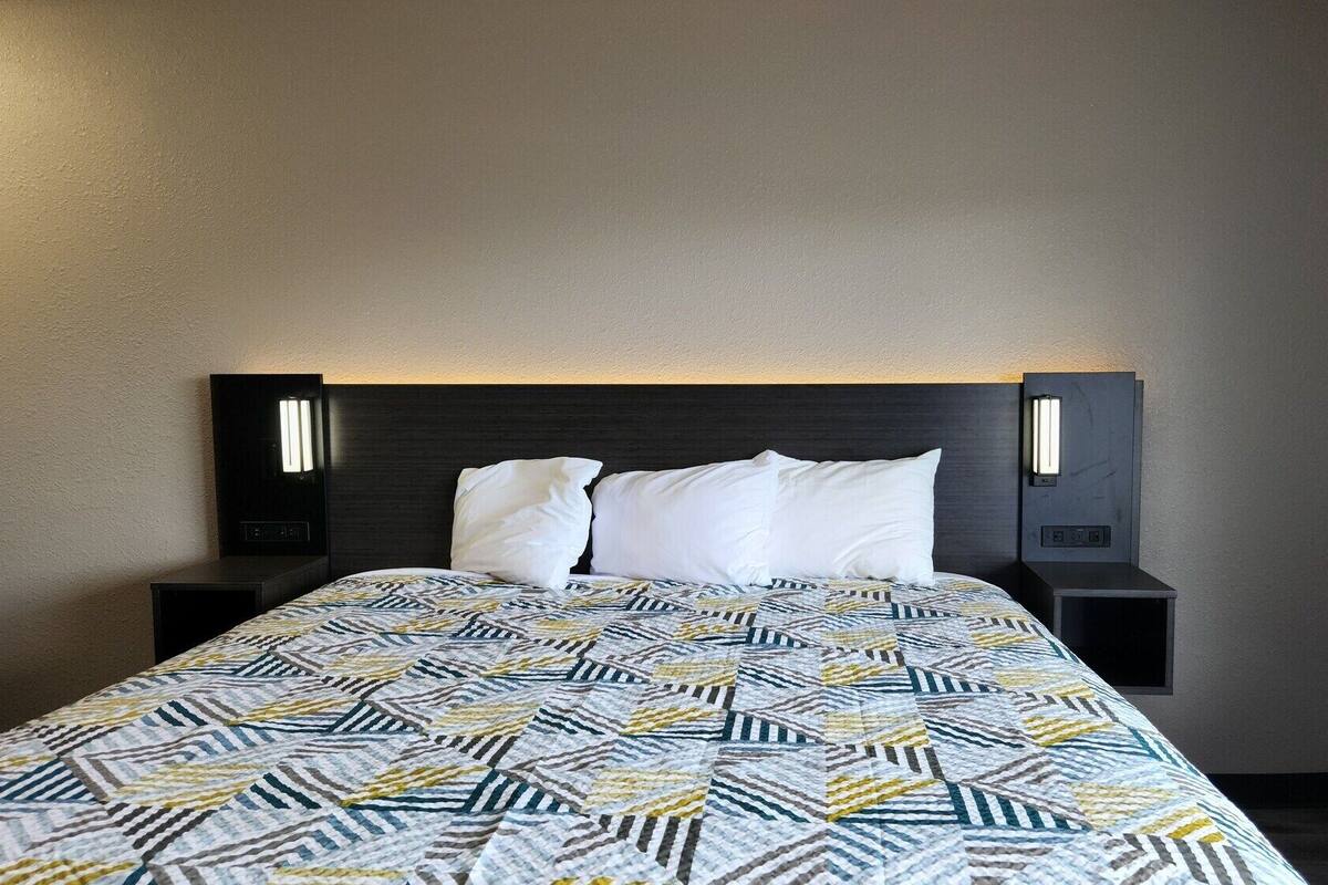 A hotel room with a bed, a headboard with integrated lighting, and a patterned bedspread.
