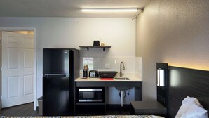 Una camera d'albergo compatta con angolo cottura, completa di frigorifero, microonde e lavandino.