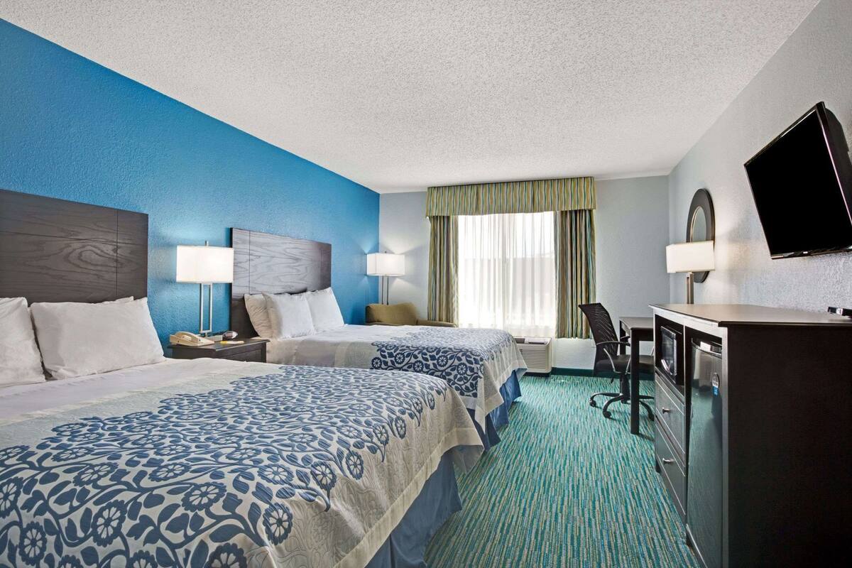 A hotel room with two beds, a desk, a TV, and a window with curtains.