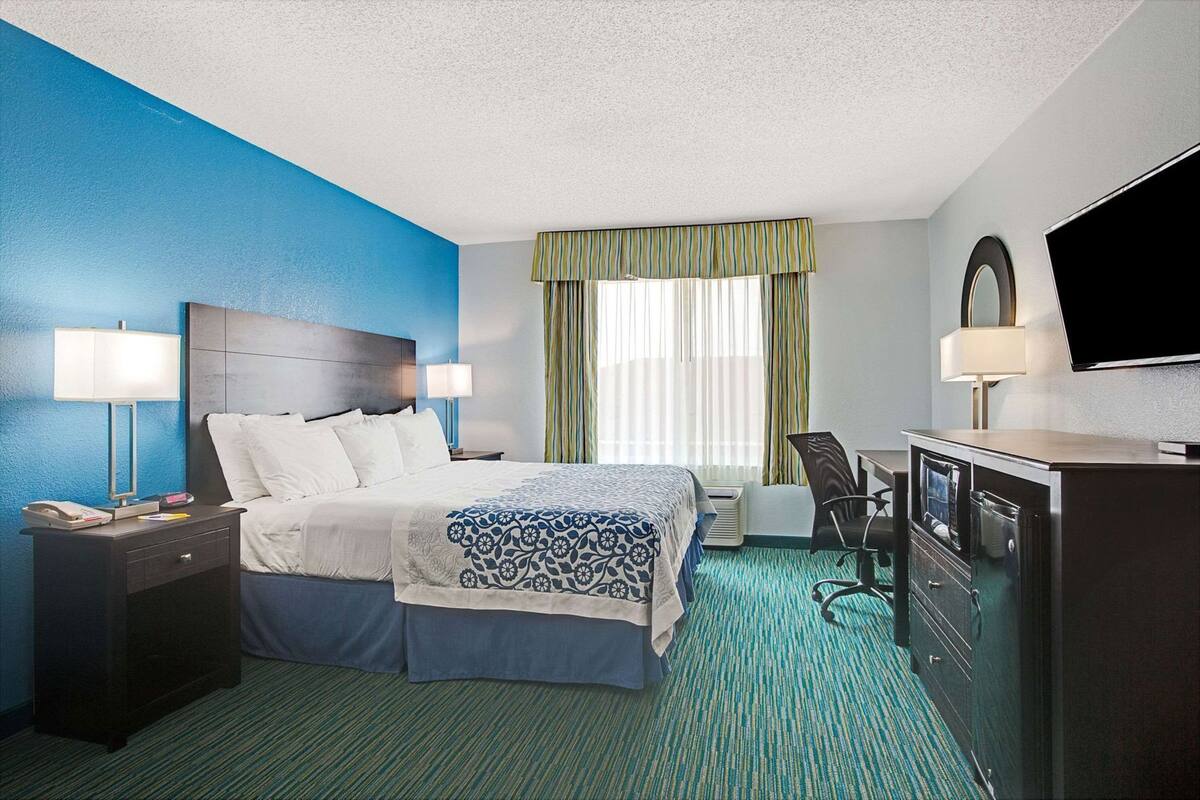 A hotel room with a bed, bedside lamps, a desk with a chair, a television, and a window with curtains.