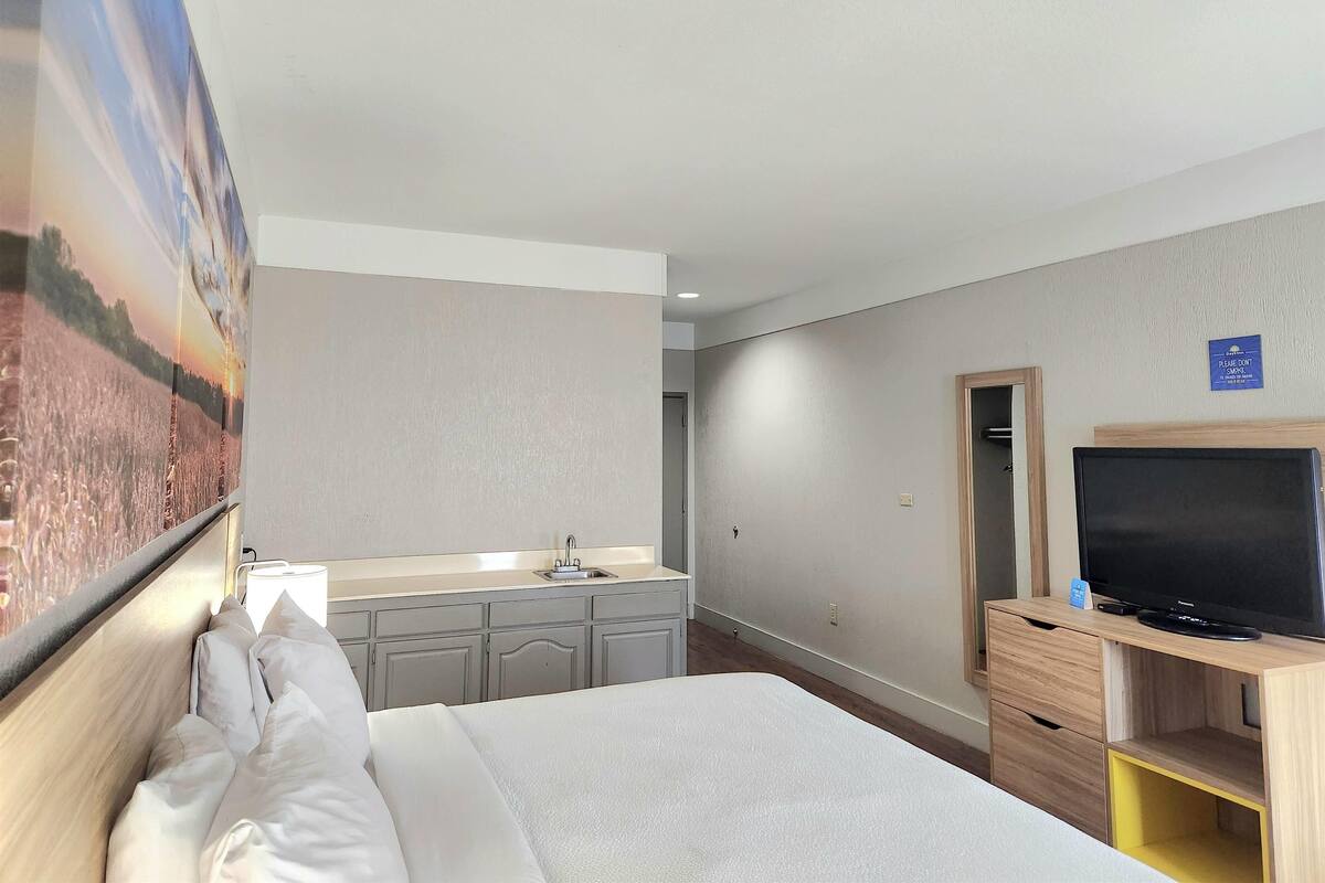 A hotel room with a bed, a TV on a wooden stand, a sink, and a mirror.