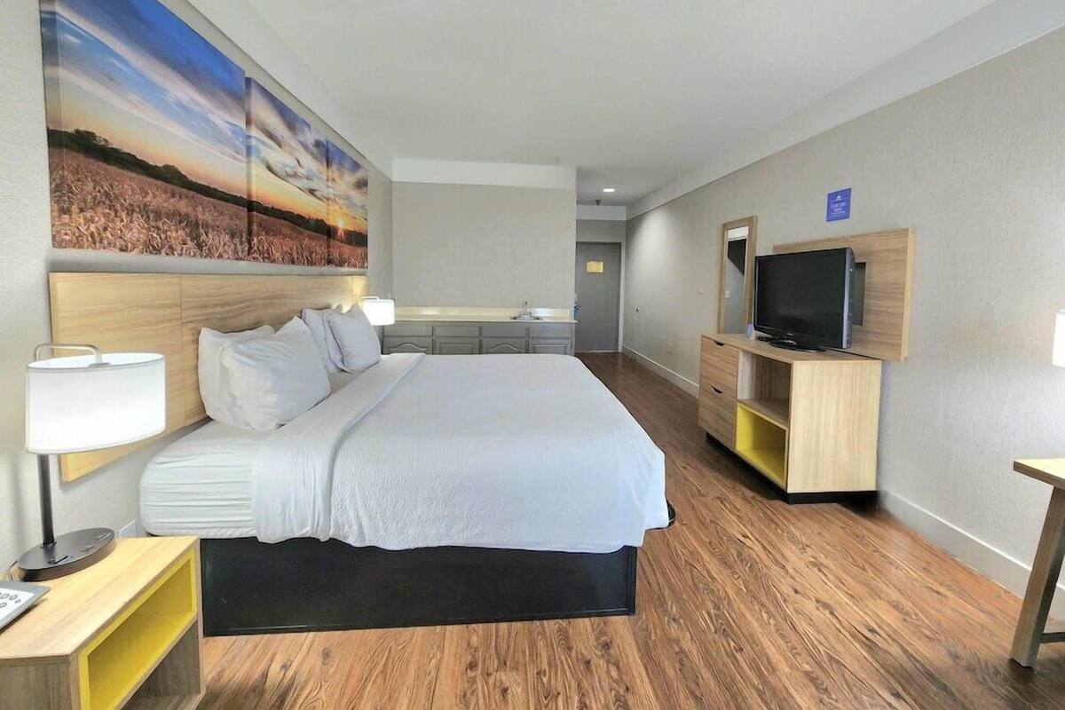 A hotel room with a large bed, a TV, a desk, and a painting on the wall.