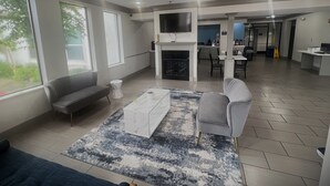 Een ruime woonkamer met een open haard, een flatscreen-televisie erboven en een eethoek op de achtergrond.
