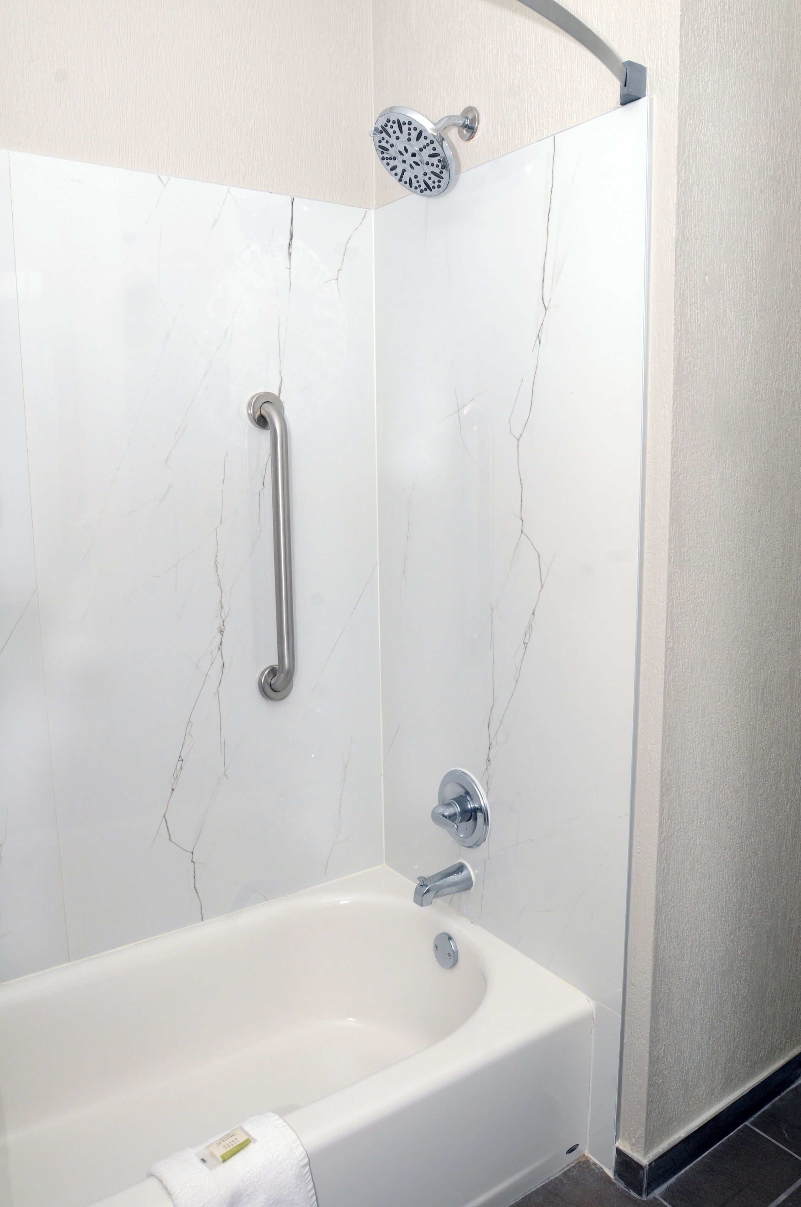 Un baño moderno con pared de mármol blanco, bañera, ducha de mano y barra de apoyo.