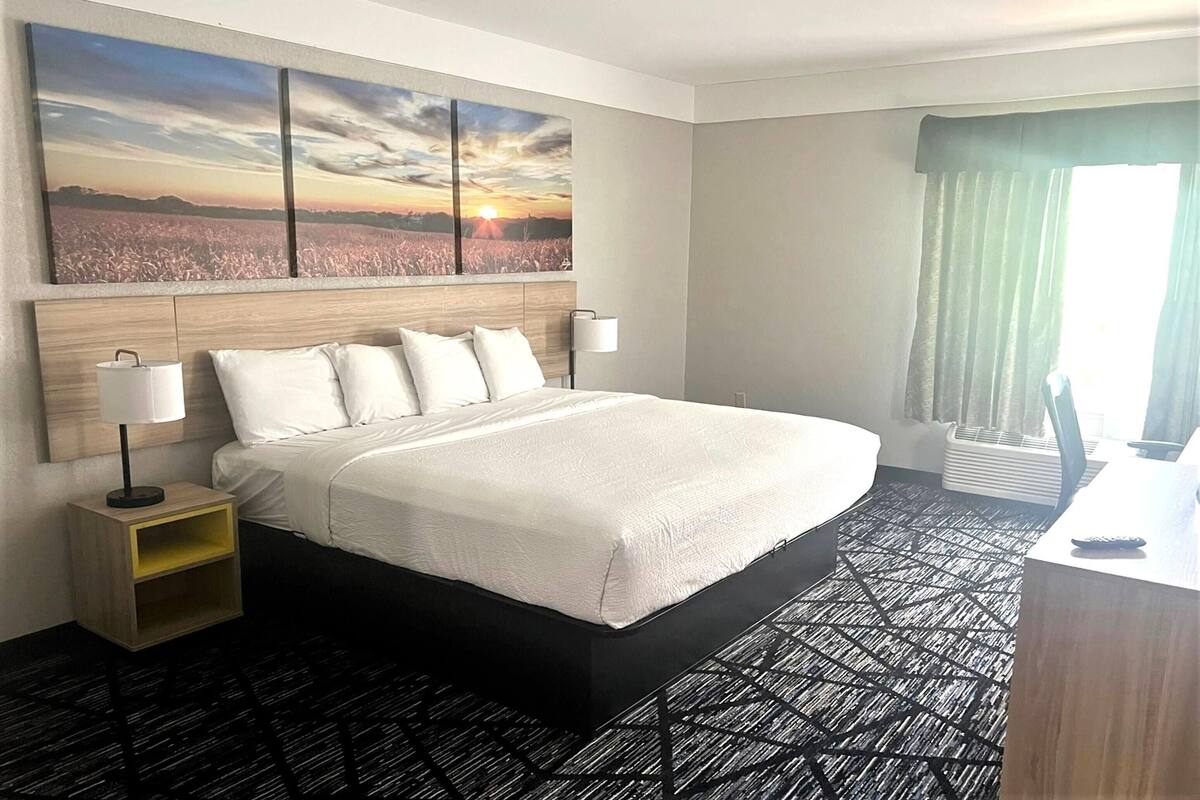 A hotel room with a large bed, two bedside tables, a desk, and a window with curtains.
