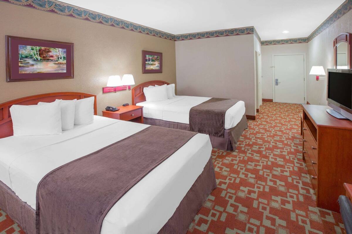 A hotel room with two beds, a TV, a desk, and two lamps.