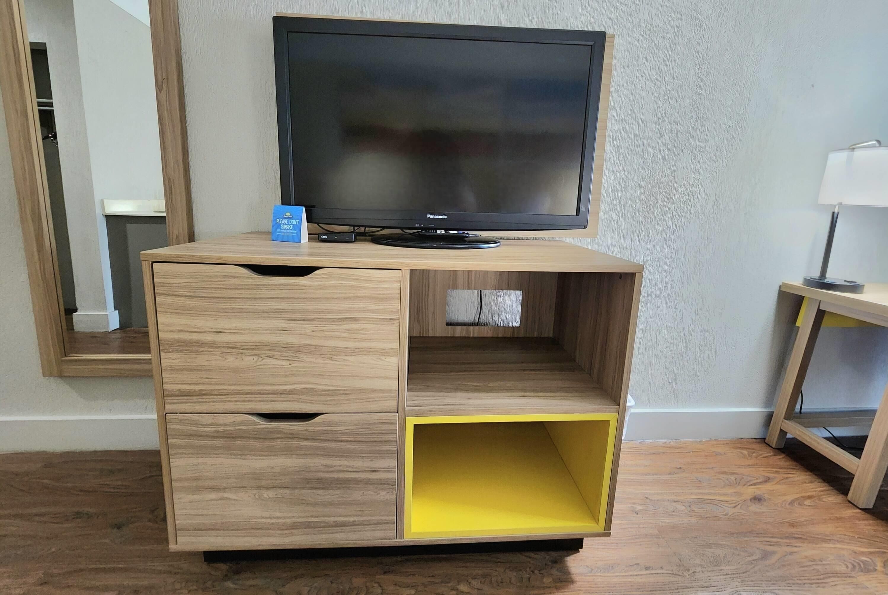 Un mueble de entretenimiento de madera con televisor de pantalla plana, cajones y un compartimento de almacenamiento amarillo.