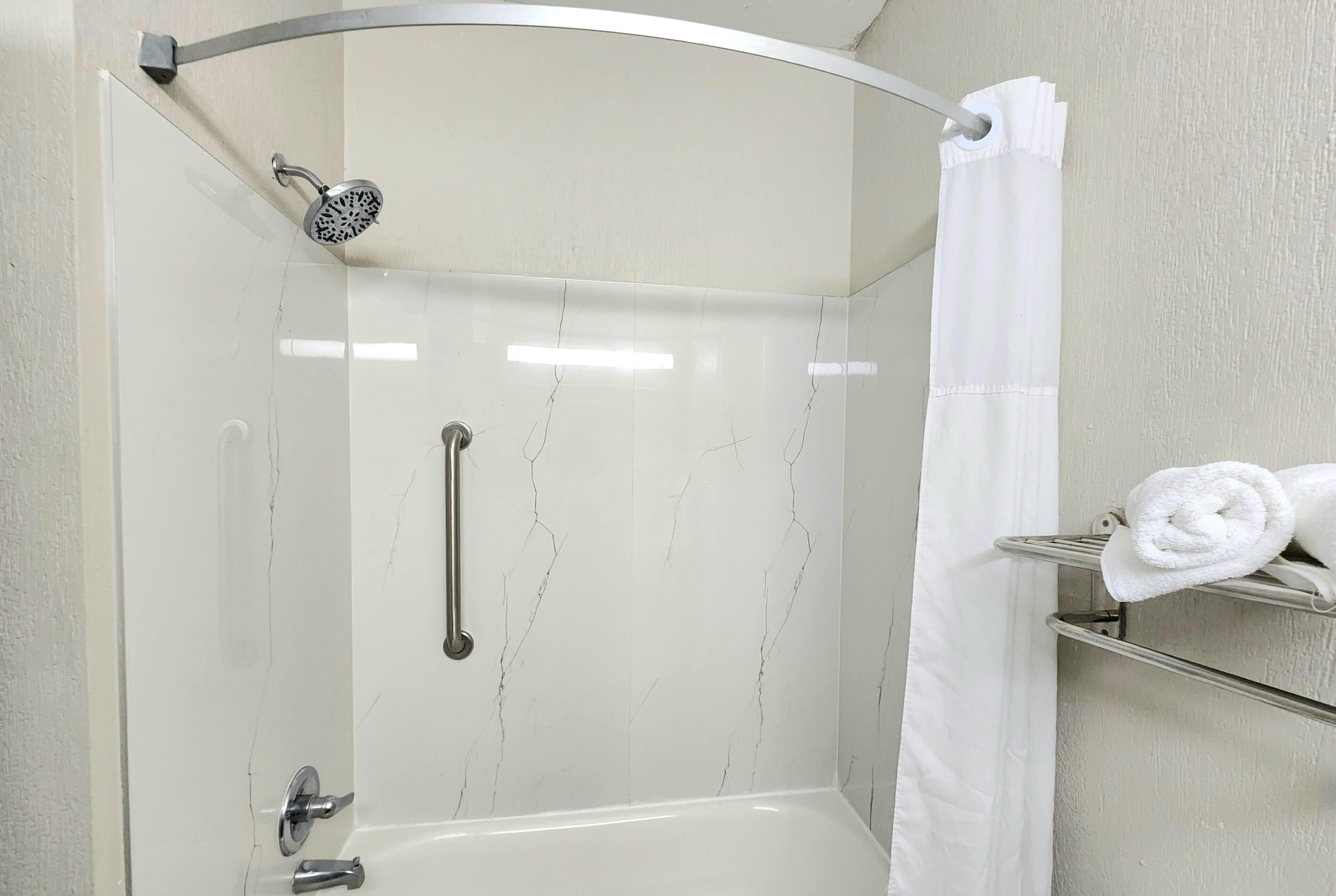 A corner shower with a handheld showerhead, a grab bar, and a towel rack with towels.