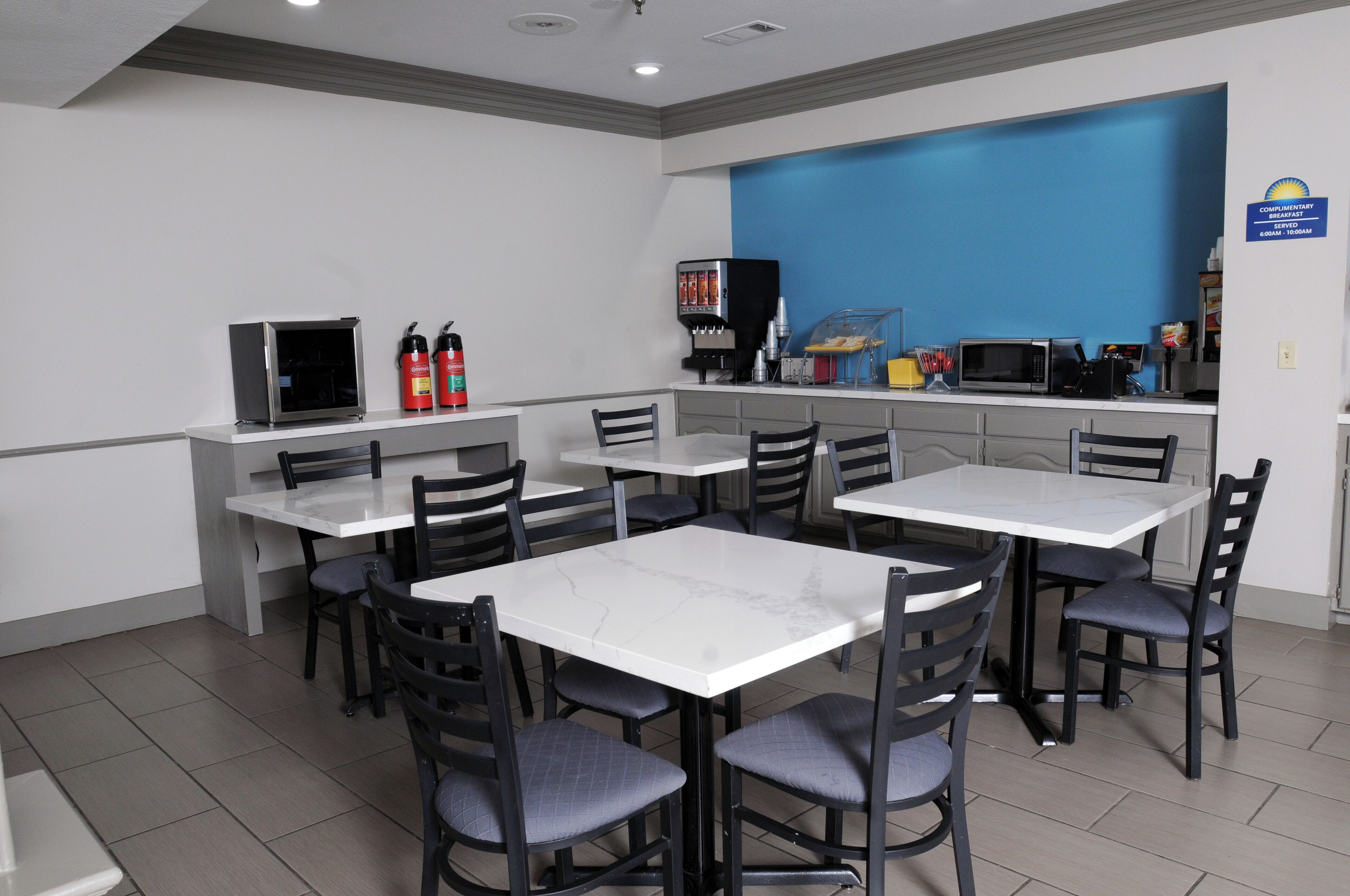 Un comedor limpio y moderno con mesas de mármol blanco y sillas negras, equipado con cafetera y microondas.