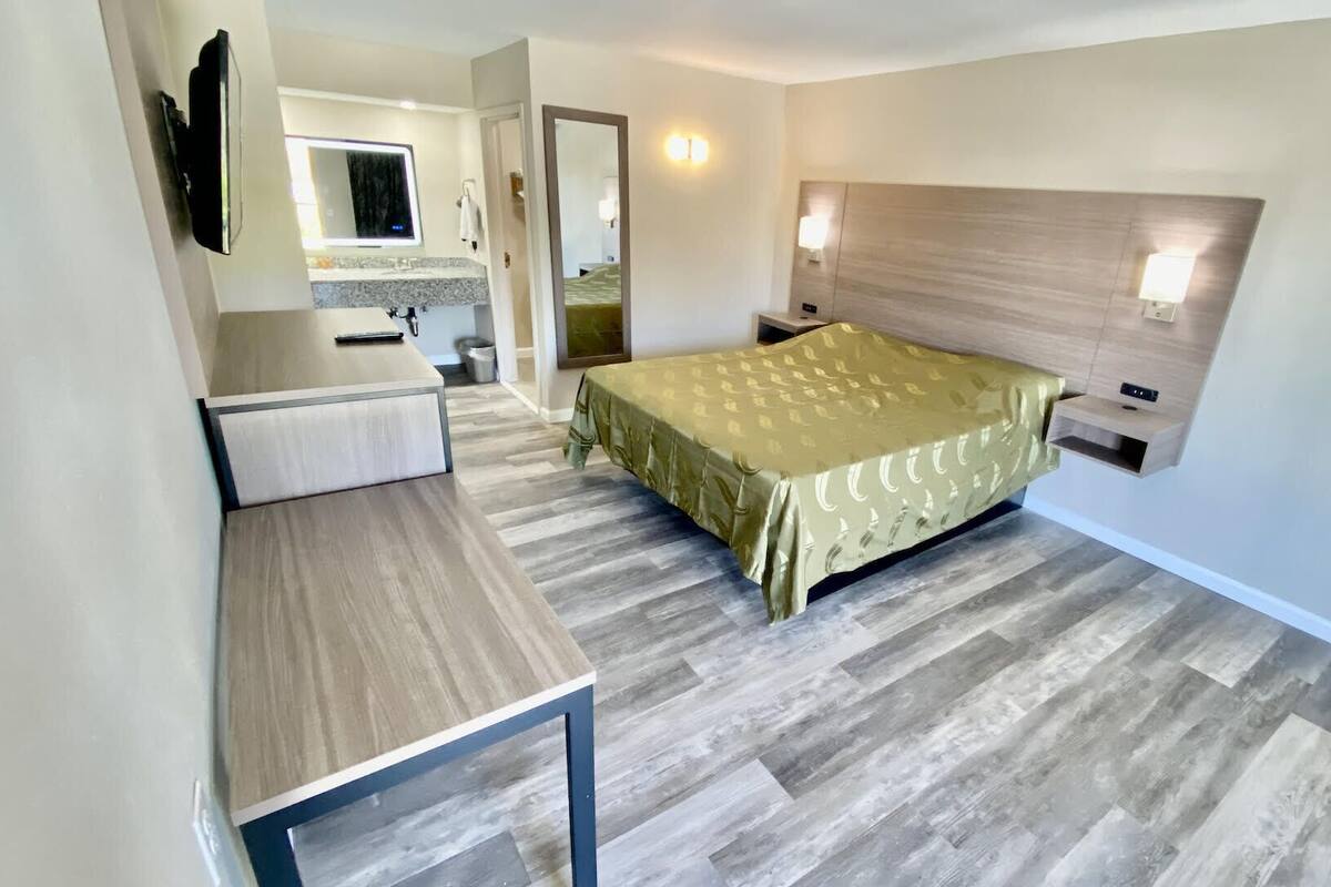 A modern hotel room with a bed, bedside table, and a small desk with a mirror.