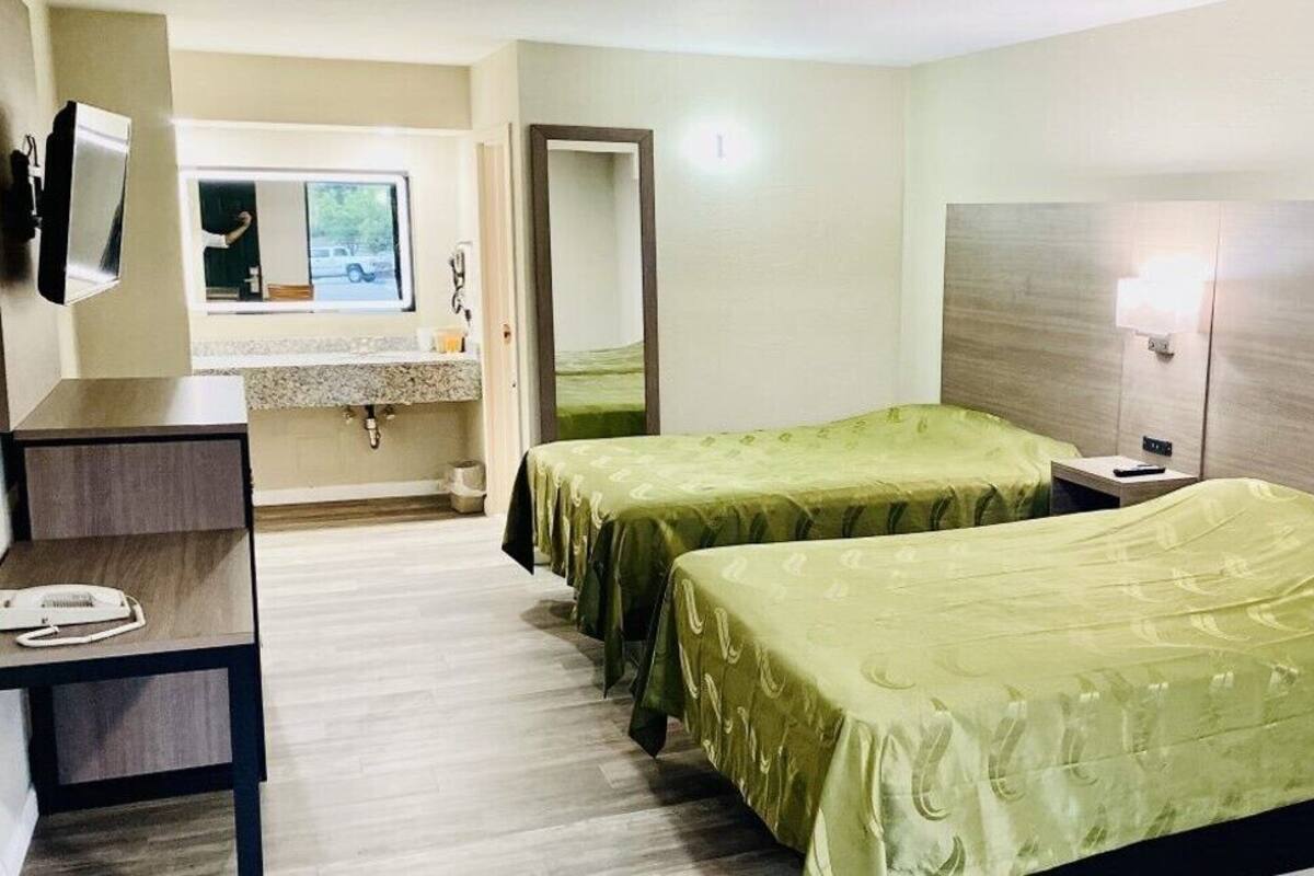 A hotel room with two single beds, a desk, a mirror, a window, and a bathroom.