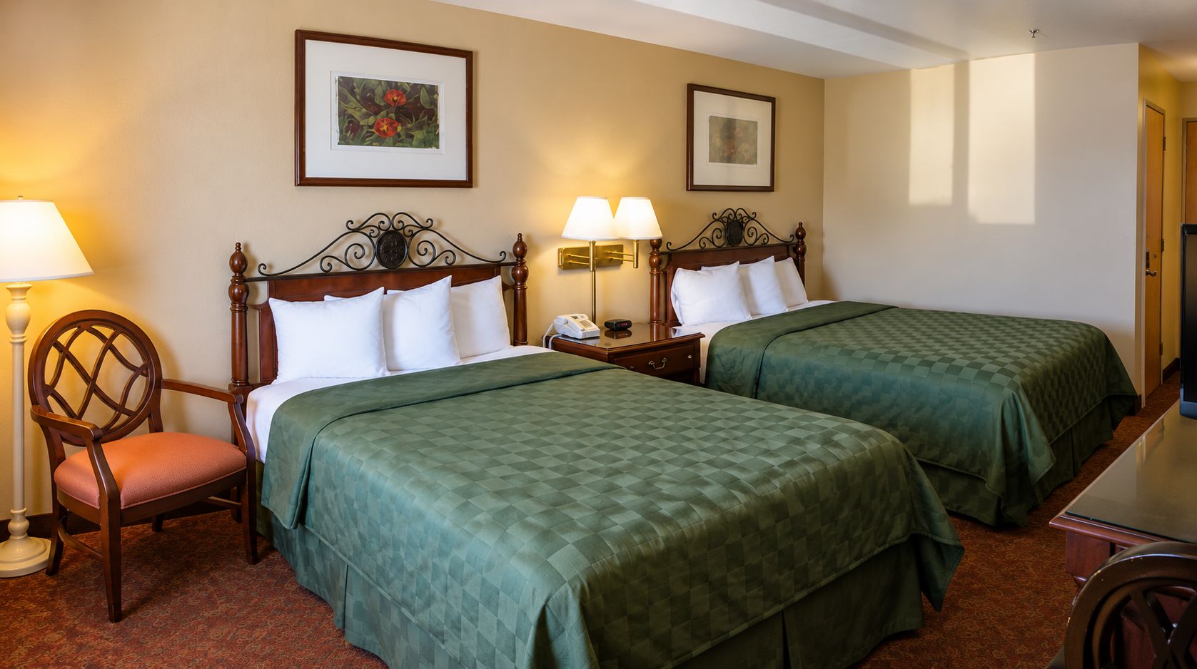 A hotel room with two beds, a chair, a nightstand, and a lamp.