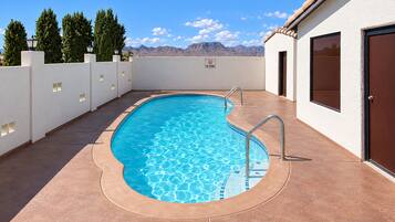A swimming pool with a no swimming sign, surrounded by a white wall and a door on the right.