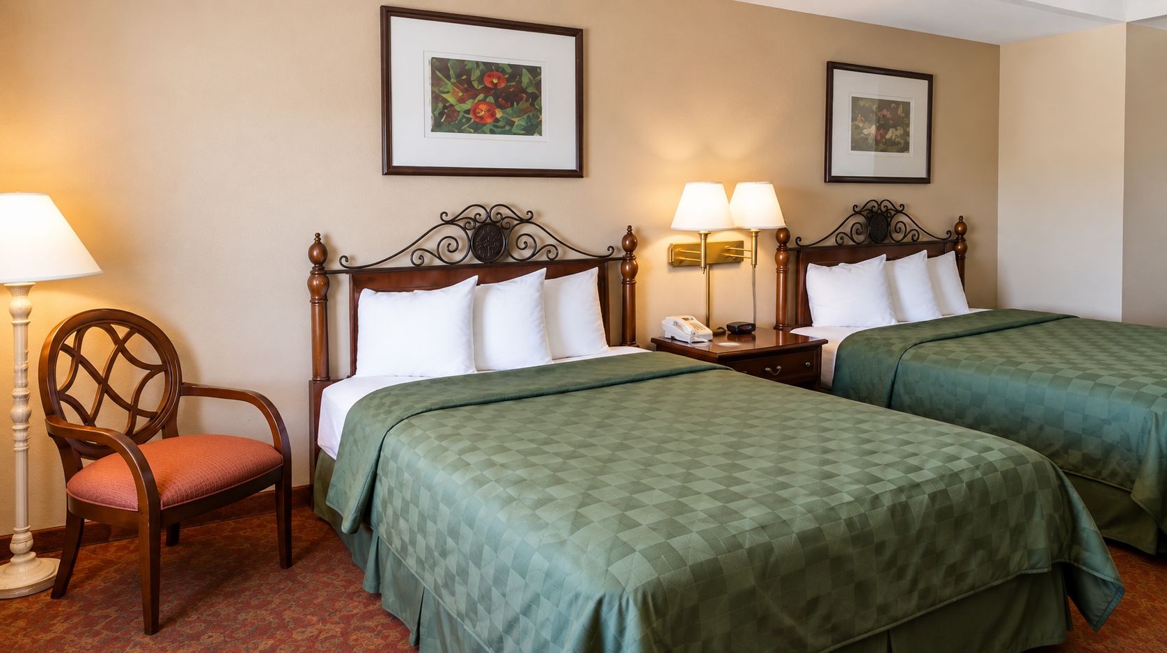 Habitación de hotel con dos camas, una silla, una lámpara y cuadros en las paredes.