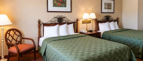 Habitación de hotel con dos camas, una silla, una lámpara y cuadros en las paredes.