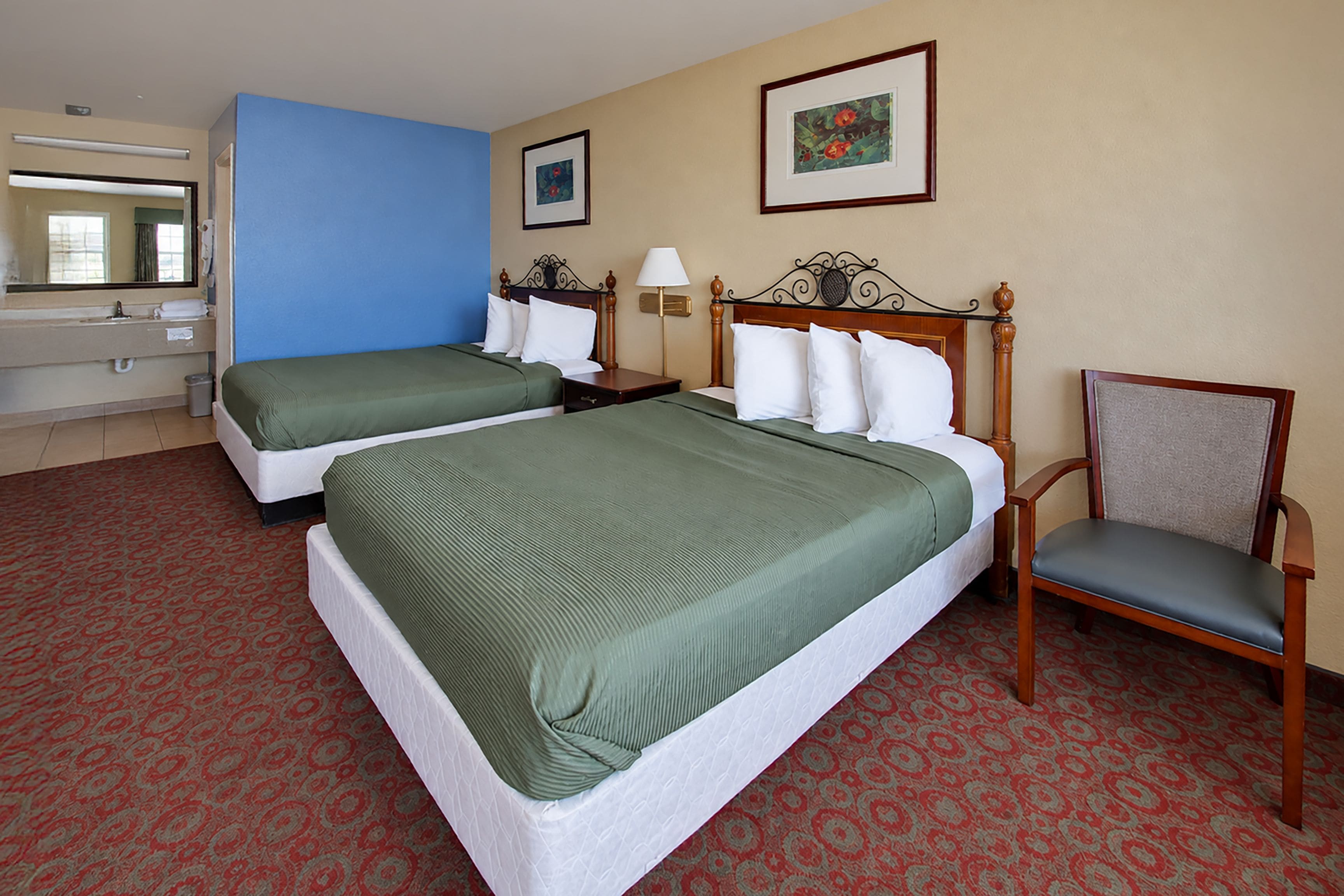 Habitación de hotel con dos camas, una silla, una mesita de noche, una lámpara y un cuadro en la pared.
