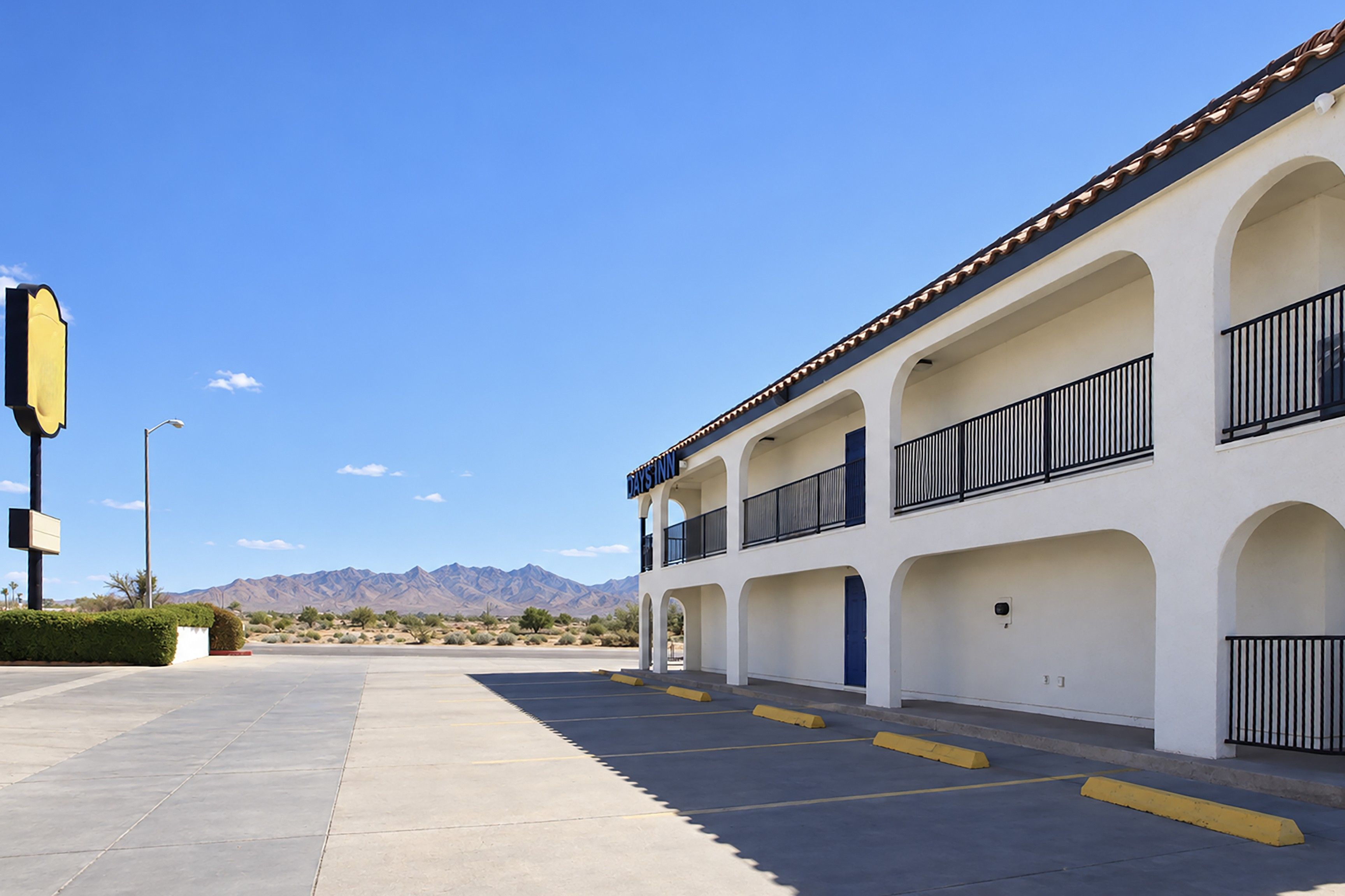 A hotel with a parking lot, multiple balconies, and a mountainous backdrop.